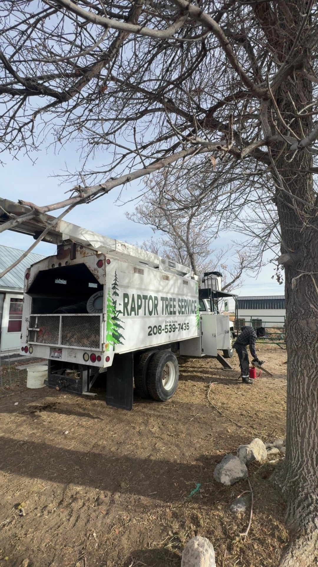 Raptor Tree Service bucket truck with the company name and phone number painted on the side, parked under bare trees in Jerome, Idaho